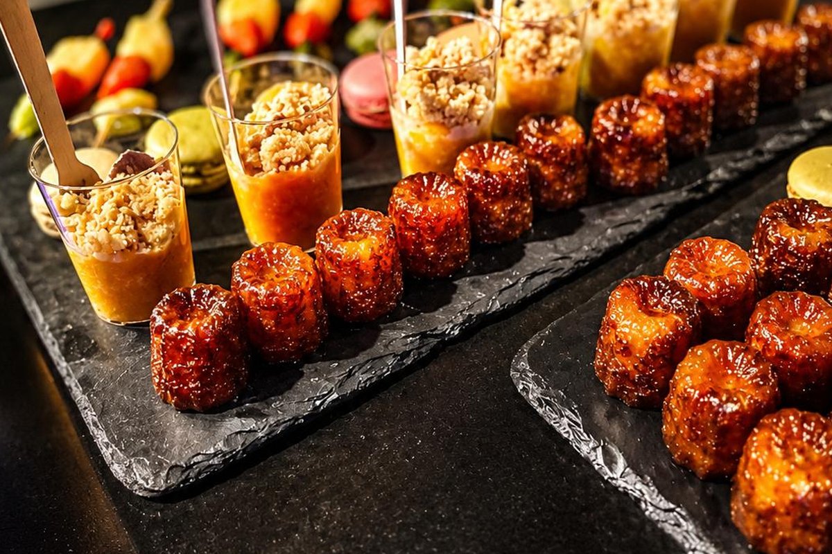 Cannelés bordelais caramélisés et verrines sucrées alignés sur ardoise